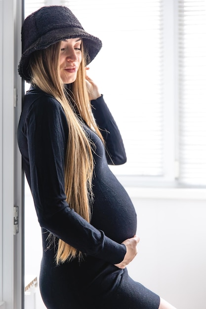 Een zwangere vrouw met lang haar in een zwarte jurk in het interieur van de kamer