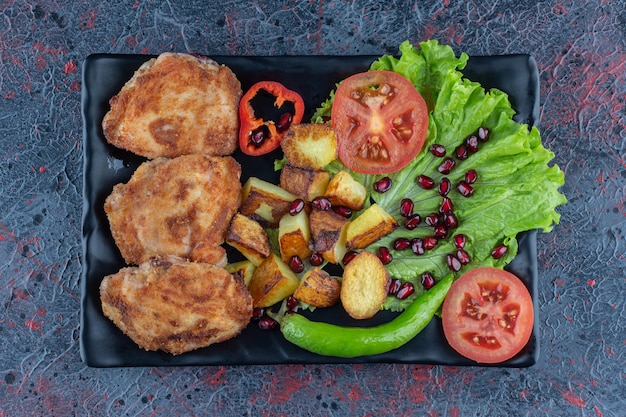 Een zwart bord met groenten en kipkoteletten