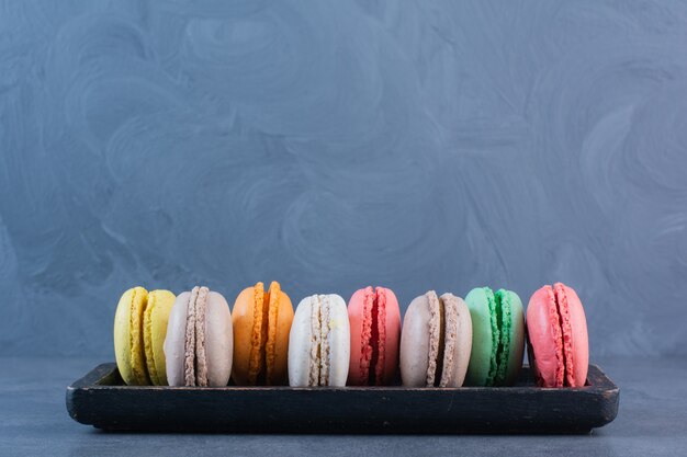 Een zwarte houten plank vol macaroni koekjes in verschillende kleuren