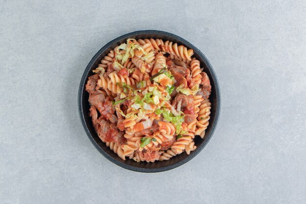 Een zwarte plaat met spiraalvormige pasta met kruiden.