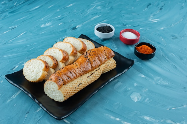 Een zwarte plaat van gesneden witbrood met kruiden op een blauwe achtergrond.