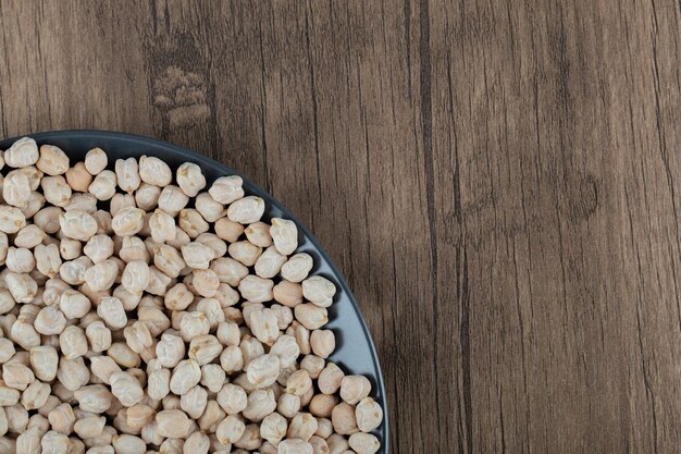 Een zwarte plaat vol gedroogde rauwe witte erwten op houten tafel.