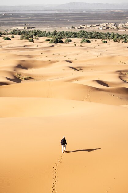 Eenzame persoon die op een zonnige dag in een woestijn in de buurt van zandduinen loopt