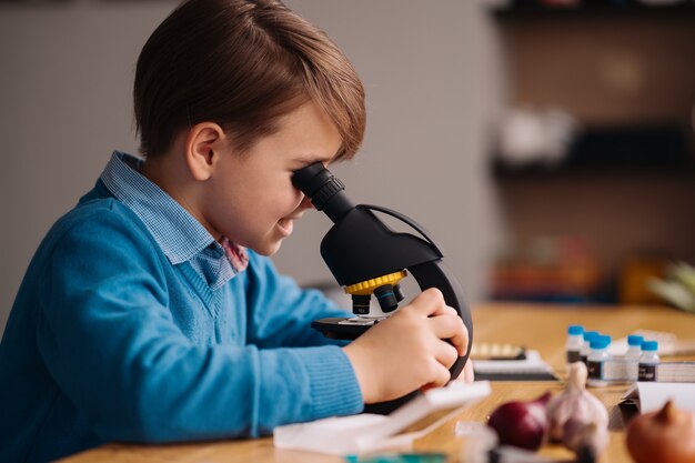 Eerste klas jongen thuis studeren met behulp van de microscoop