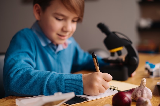 Eerste klas jongen thuis studeren met behulp van de microscoop