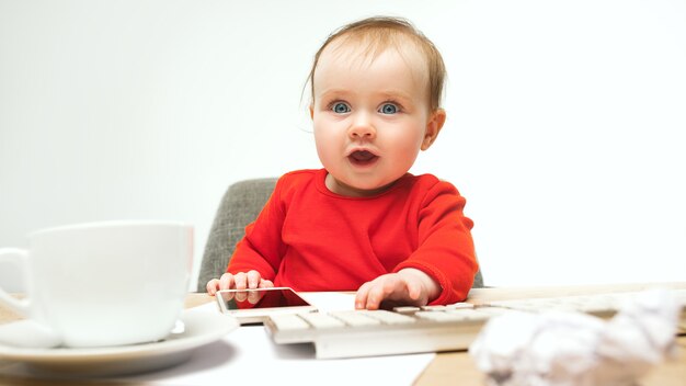 Eerste sms. Kind babymeisje zit met toetsenbord van moderne computer of laptop in het wit