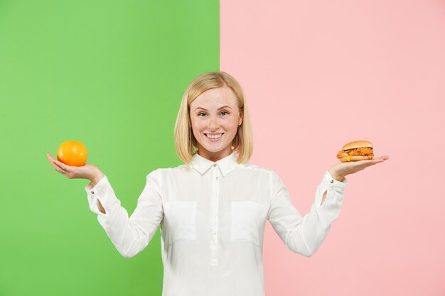 Eetpatroon. Dieet concept. Gezond eten. Mooie jonge vrouw kiezen tussen fruit en ongelofelijk fastfood