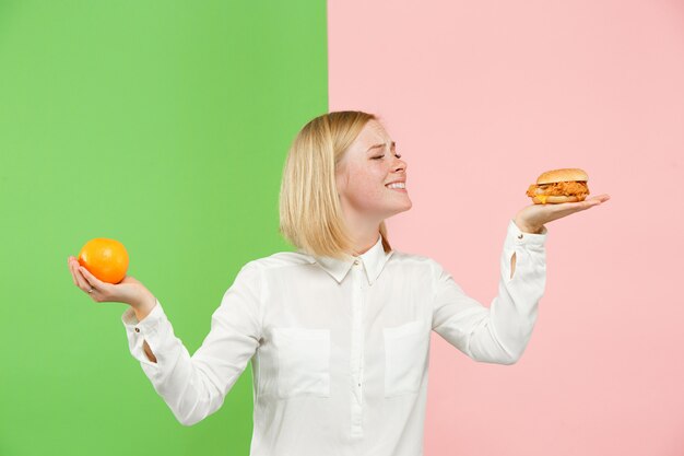 Eetpatroon. Dieet concept. Gezond eten. Mooie jonge vrouw kiezen tussen fruit en ongelofelijk fastfood