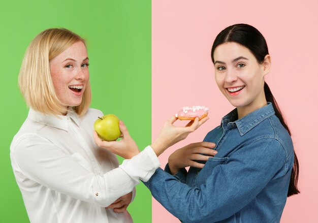 Eetpatroon. Dieet concept. Gezond, nuttig voedsel. Mooie jonge vrouwen die tussen fruit en unhelathy cake bij studio kiezen. Menselijke emoties en vergelijkingsconcepten
