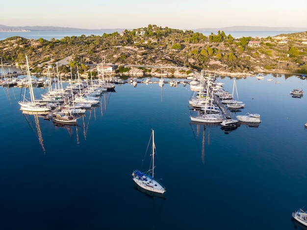 Gratis foto egeïsche zeehaven met meerdere afgemeerde jachten in de buurt van pieren, groen, blauw water, uitzicht vanaf de drone, griekenland