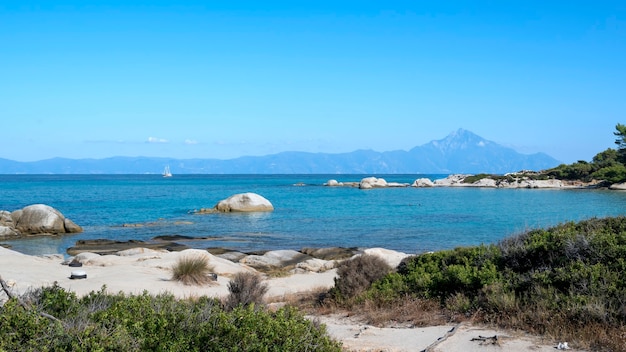 Gratis foto egeïsche zeekust met zwemmende mensen, rotsen over het water en land met boot in de verte, groen op de voorgrond, blauw water, griekenland