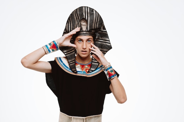 Gratis foto egyptische man farao in oud egyptisch kostuum kijkend naar de voorkant, verward en verrast terwijl hij over een witte muur staat
