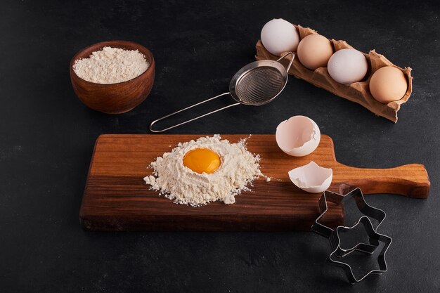 Ei en bloem met elkaar vermengd op een houten bord met rondom koekjesvormen.