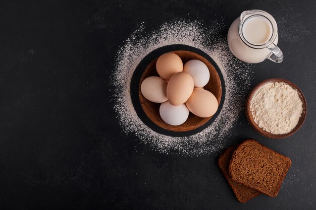 Eieren in een houten beker met een pot melk opzij, bovenaanzicht.