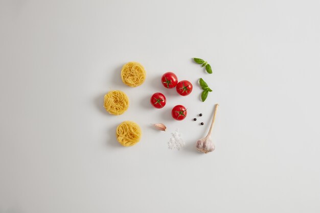 Eierpasta nesten, tomaten, knoflook, basilicumblaadjes, zeezout voor het maken van heerlijke pasta. Traditioneel Italiaans gerecht. Voedsel met veel calorieën. Voedende ongekookte noedels en verse groenten