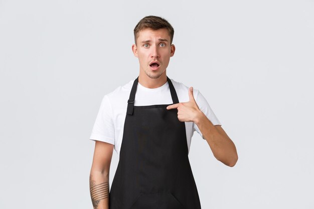 Eigenaren van kleine bedrijven, coffeeshop en personeelsconcept. Bezorgde en verwarde domme barista, ober die wordt beschuldigd of beschuldigd, zichzelf verbaasd wijzend, staande op een witte achtergrond