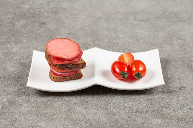 Eigengemaakte sandwich en tomaat op witte plaat.