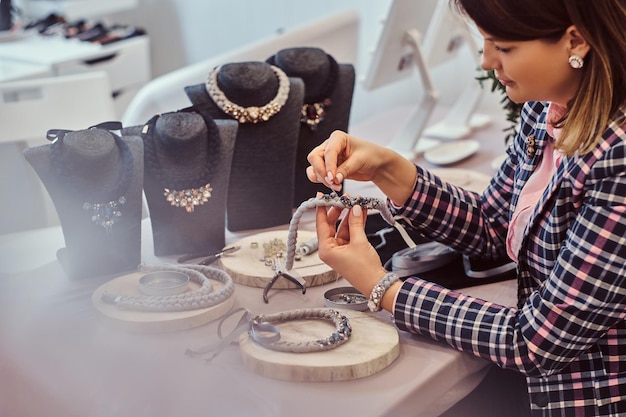 Elegant geklede vrouw maakt handgemaakte kettingen, werken met naalden en draad in sieraden workshop.