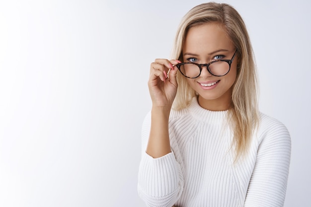 Elegante blonde zakenvrouw die een bril afdoet en naar de camera kijkt met een tevreden en zelfverzekerde blik glimlachend brutaal wetende manieren om te slagen hoe zaken te leiden, gemakkelijk financiële vragen te behandelen.