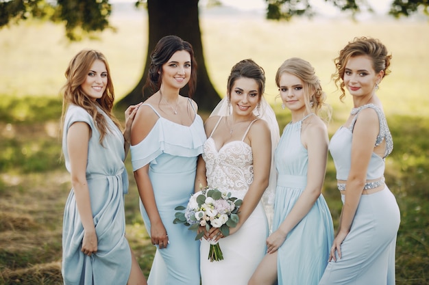 Elegante en stijlvolle bruid samen met haar vier vrienden in blauwe jurken staan ​​in een park