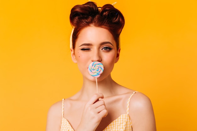 Elegante gember meisje likt lolly. Vooraanzicht van enthousiaste vrouw met hard snoep.