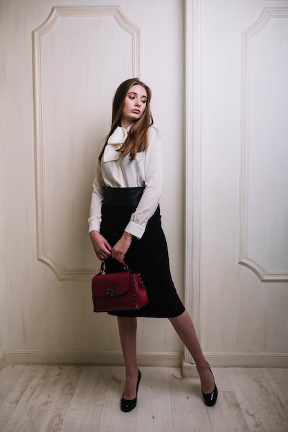 Elegante jonge vrouw in rok en blouse met handtas in de kamer