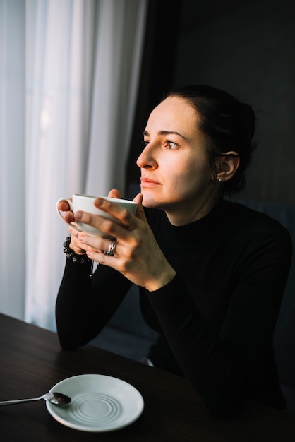 Elegante jonge vrouw met een kopje drank aan tafel