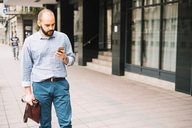 Elegante man die straat met smartphone loopt