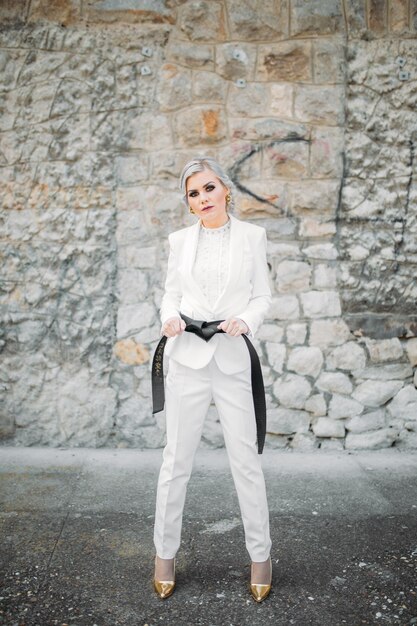 Elegante modieuze vrouw in een wit pak met zwarte riem en broek poseren voor mode fotoshoot