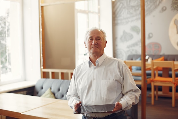 Elegante oude man in een café met behulp van een laptop