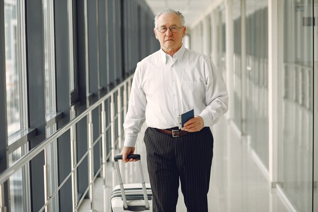 Elegante oude man op de luchthaven met een koffer