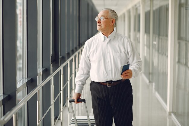 Elegante oude man op de luchthaven met een koffer