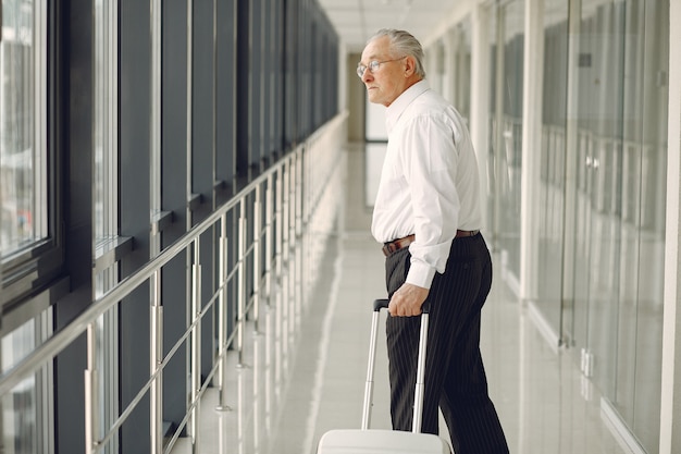 Elegante oude man op de luchthaven met een koffer