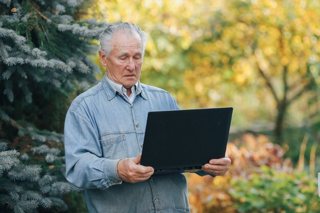 Elegante oude mens die zich op grijze achtergrond bevindt en laptop met behulp van