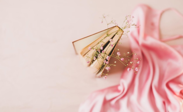 Elegante roze jurk en een boek met bloemen op beige achtergrond