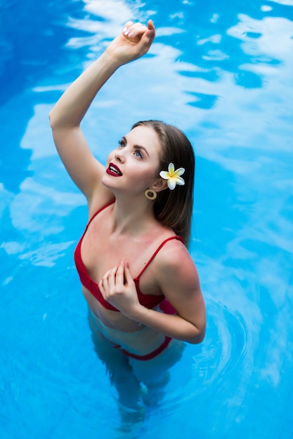 Elegante sexy vrouw in de rode bikini op het zongebruinde slanke en welgevormde lichaam zwemmen in het zwembad