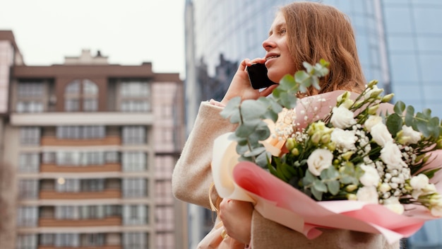 Elegante vrouw buiten praten aan de telefoon en boeket bloemen te houden