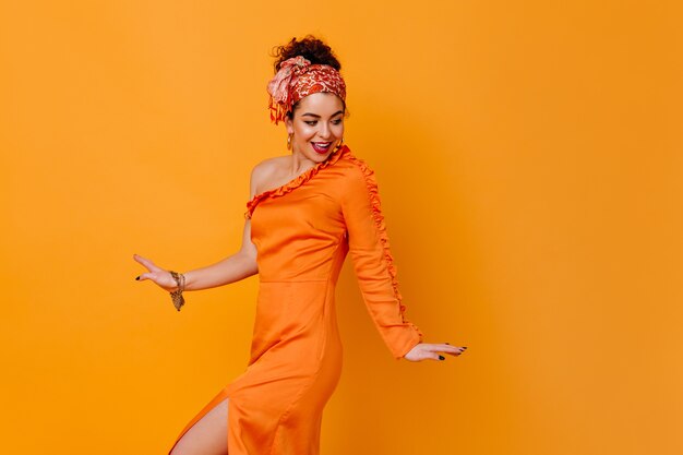 Elegante vrouw in jurk met blote schouder coquettishly poseren op oranje ruimte.