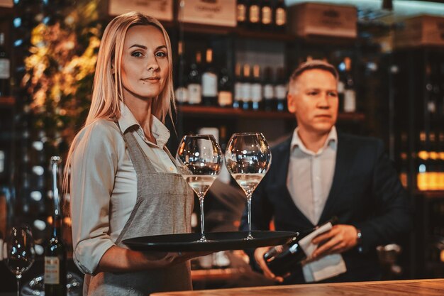 Elegante wijnsommelier en zijn aantrekkelijke assistent staan klaar om nieuwe wijn te proberen in een privé wijnboetiek.