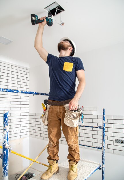 Elektricien Bouwer aan het werk, installatie van lampen op hoogte. Professioneel in overall met een boormachine op de achtergrond van de reparatielocatie.