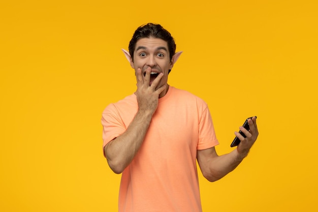 Elfenkerel opgewonden knappe schattige kerel in oranje t-shirt die gelukkig telefoon vasthoudt