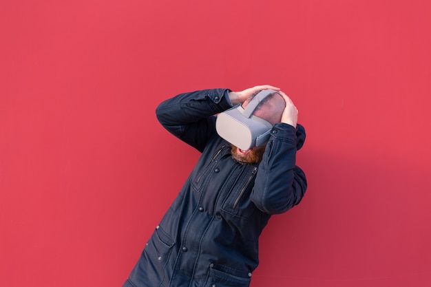 Gratis foto emotioneel portret van een man op straat met een realiteitsbril tegen de achtergrond van een rode muur