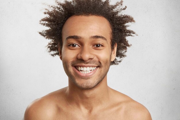Emotionele blije glimlachende man heeft een aantrekkelijk uiterlijk, borstelige afro-haarstijl, witte, gelijkmatige tanden