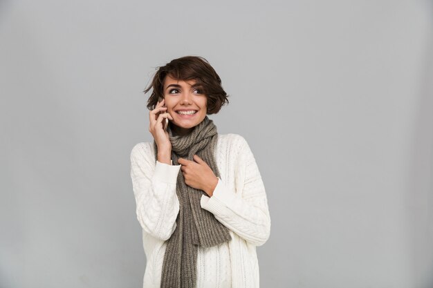 Emotionele jonge dame die sjaal draagt die door mobiele telefoon spreekt.