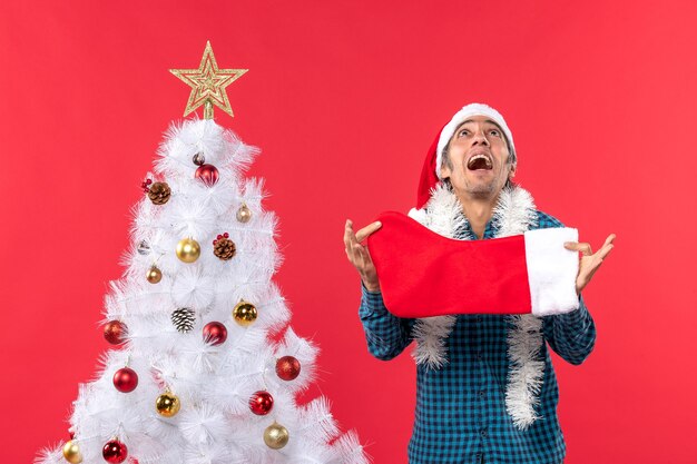 Emotionele jonge man met kerstman hoed in een blauw gestript shirt en kerst sok te houden op zoek naar boven