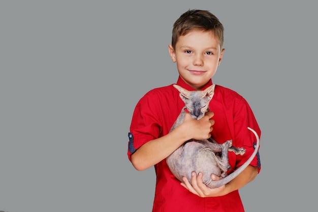 Emotionele kleine jongen in een rood polot-shirt houdt een kat vast. Geïsoleerd op grijze achtergrond.