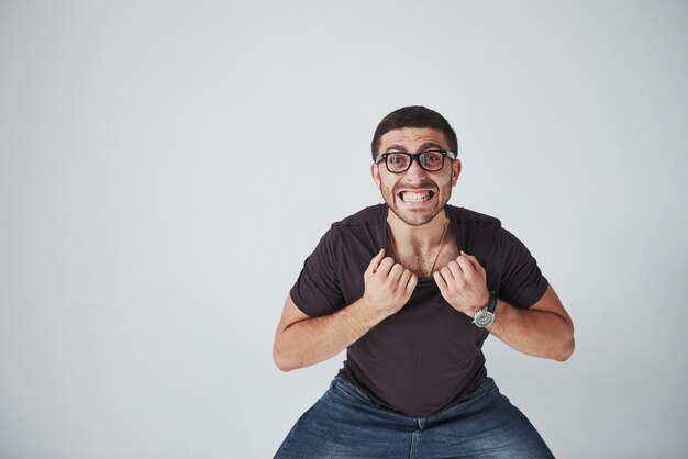 Emotionele man in casual kleding en met een bril houdt zichzelf vast aan de kraag van een T-shirt