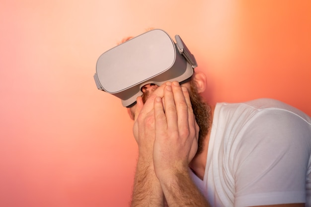 Emotionele portret van een man met een baard met een virtual reality-bril in de studio op een roze oranje achtergrond