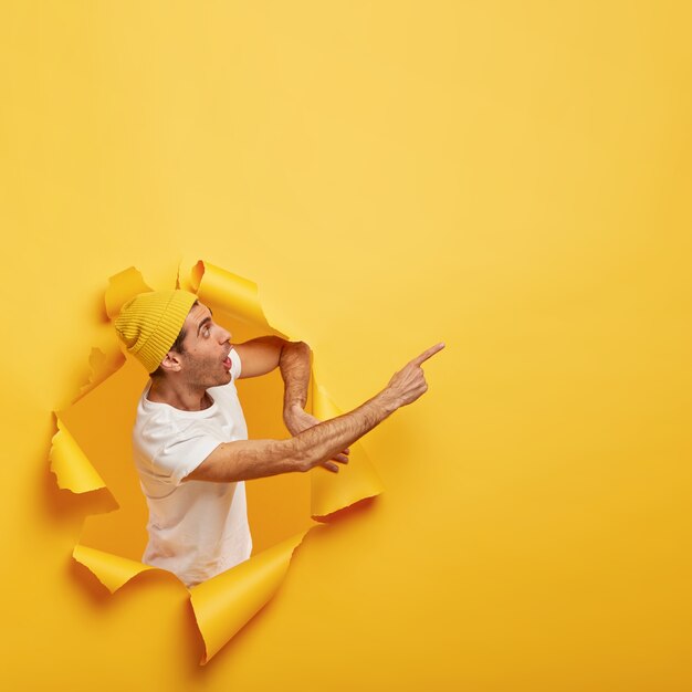 Emotionele verrast man staat in papiergat met gescheurde gele randen, toont ongelooflijke kopie ruimte