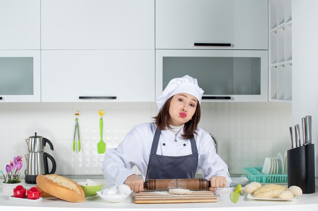 Emotionele vrouwelijke commischef in uniform die achter tafel staat en gebak bereidt in de witte keuken